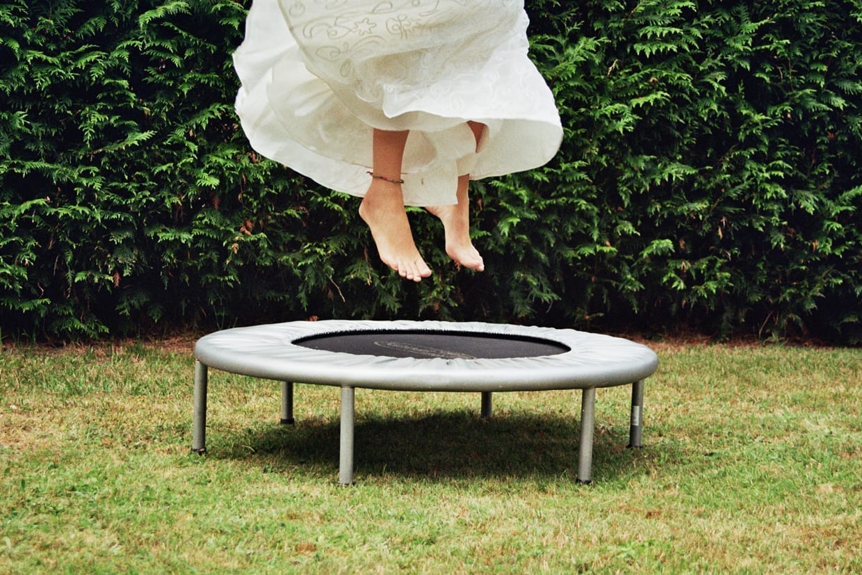 A woman wearing a dress jumping on a trampoline.