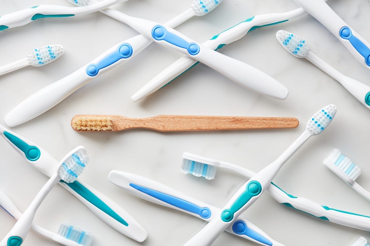 Top view of organic bamboo toothbrush lying amongst plastic alternatives on white background.