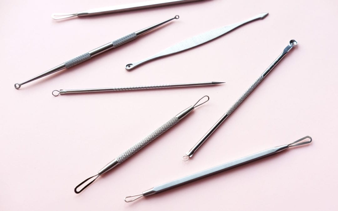 Tools for removing acne on a pink background.