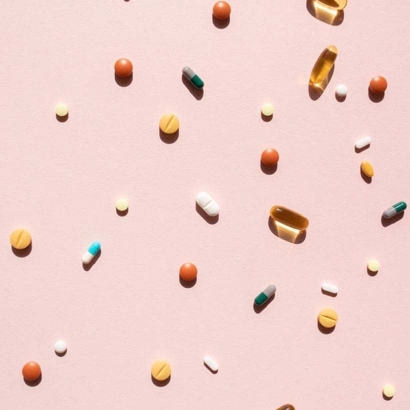 Top view of various pills and tablets on a pink background.