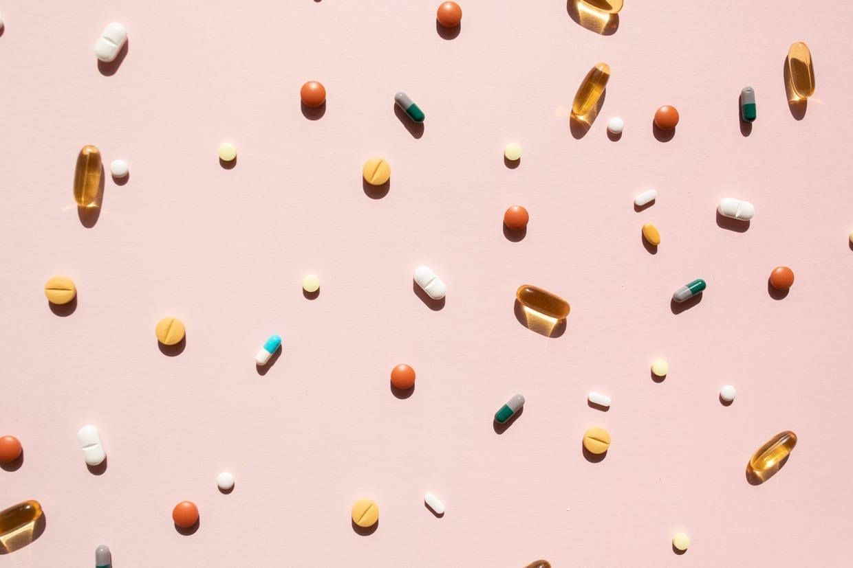 Top view of various pills and tablets on a pink background.