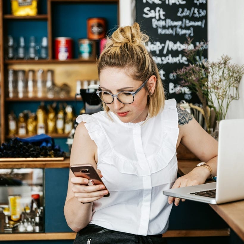 Stylish, tattooed young woman is working at a cafe and checking her messages on her smartphone.