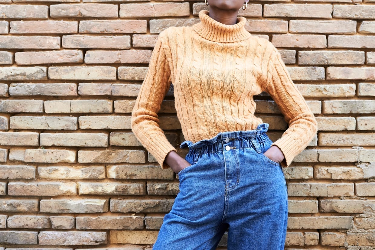 Crop of faceless fashionable woman wearing yellow neck jumper against brick wall.