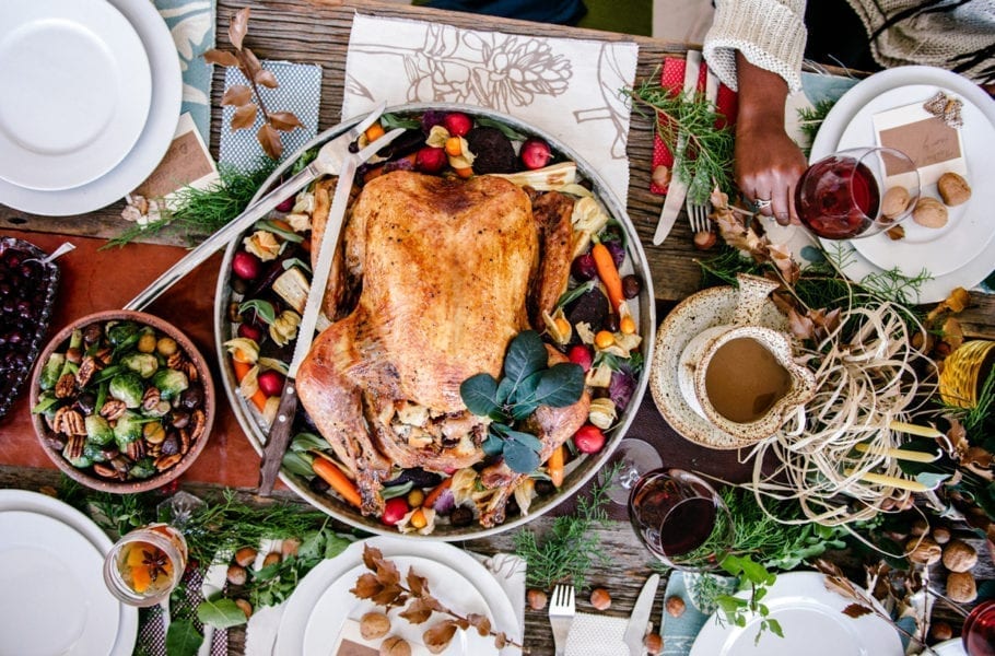 Overhead view of a Thanksgiving dinner set on a table with a turkey, side dishes and wine.