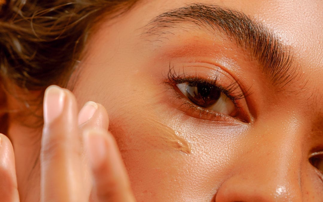 A woman applies a serum to her face.