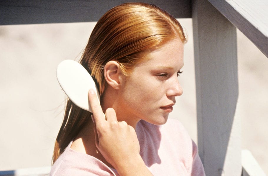 Young woman sitting on a balcony brushing her hair.