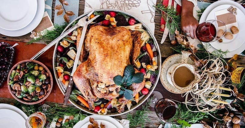 Overhead view of a Thanksgiving dinner set on a table with a turkey, side dishes and wine.