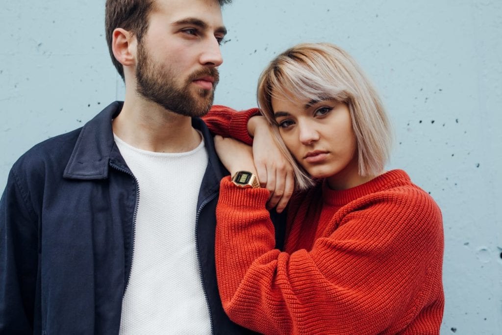 Couple standing against a blue background looking at the camera.