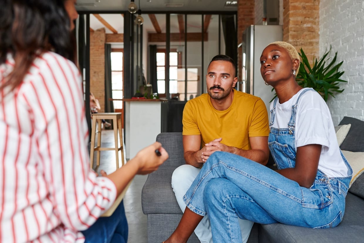 Diverse young couple sitting on their sofa at home having a session with a marriage counselor.