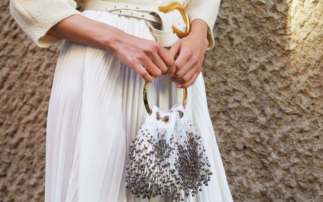 Close up of a woman in a white skirt and cream blouse holding a small jeweled purse.