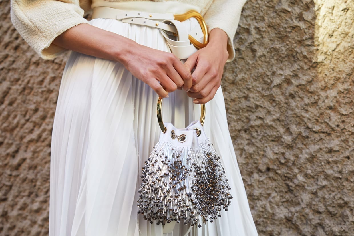 Close up of a woman in a white skirt and cream blouse holding a small jeweled purse.
