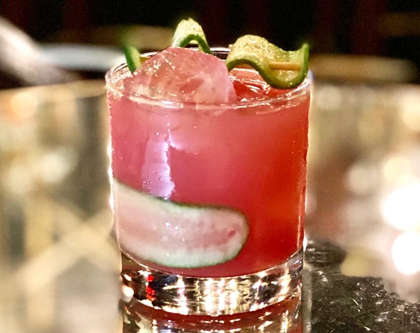 A pink cocktail with cucumber slices.