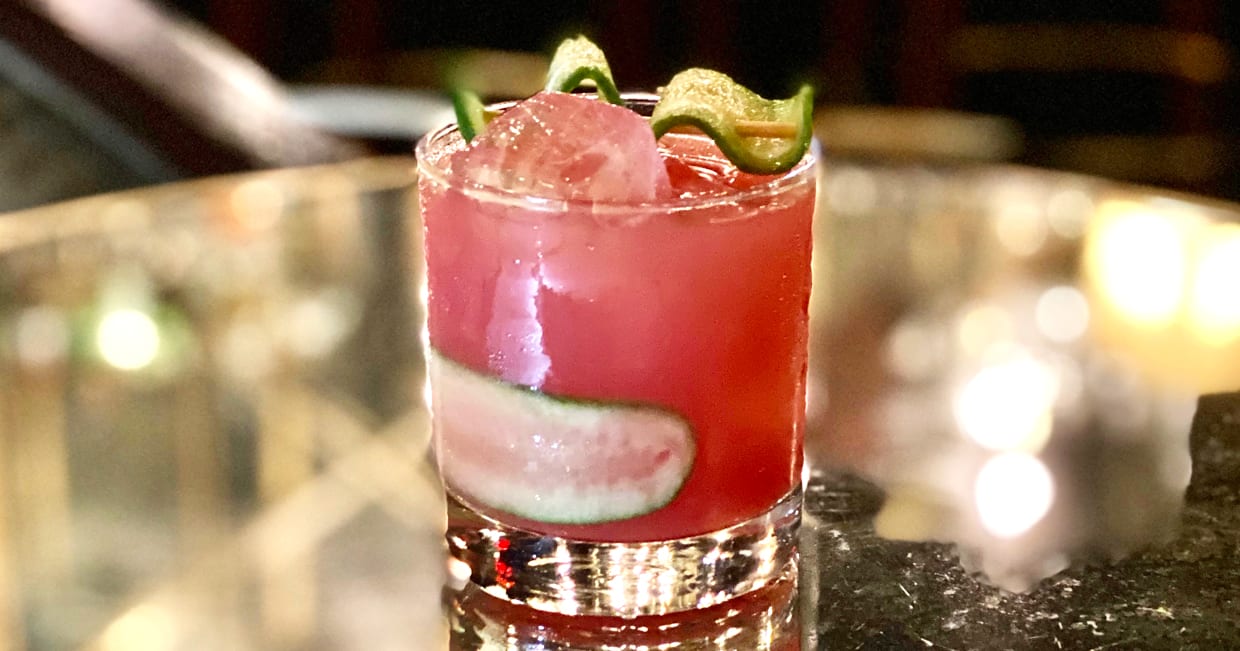 A pink cocktail with cucumber slices.
