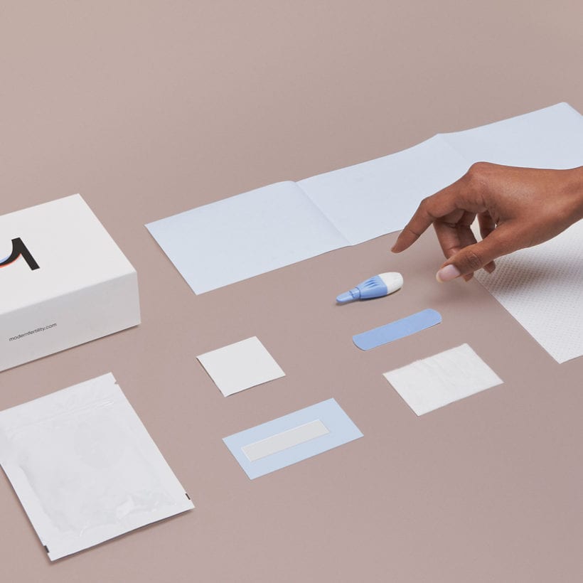 A flat lay of the Modern Fertility test kit with a hand reaching in.