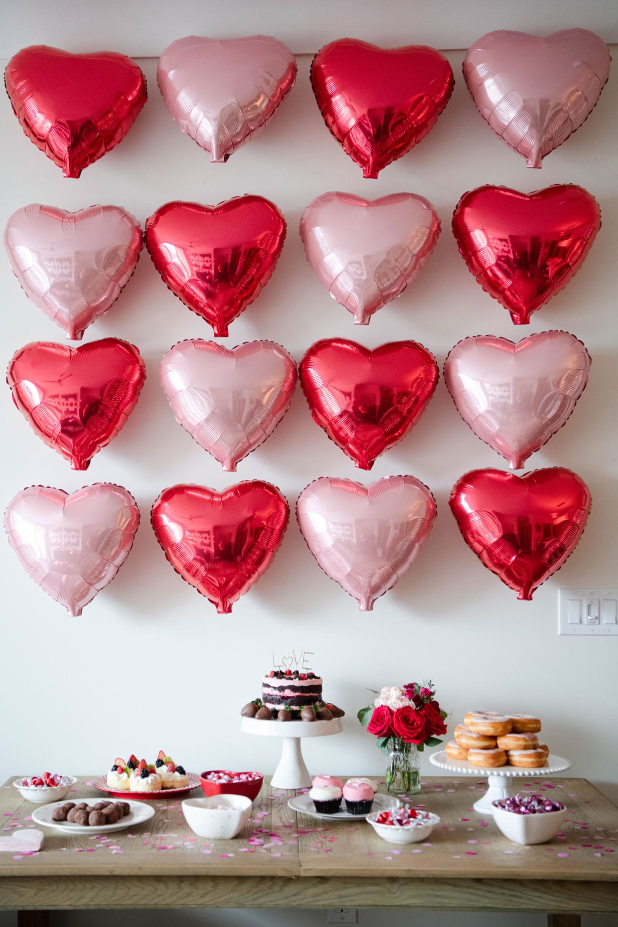 A table set with desserts in front of a pink and red heart wall.