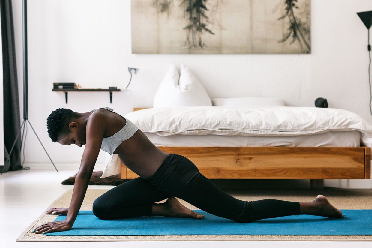 A black woman doing hatha yoga exercises on the floor in a bedroom.