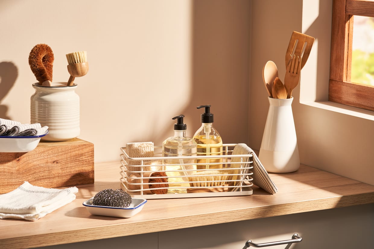 A collection of assorted eco friendly sponges and brushes places on cupboard near natural detergents in modern kitchen.