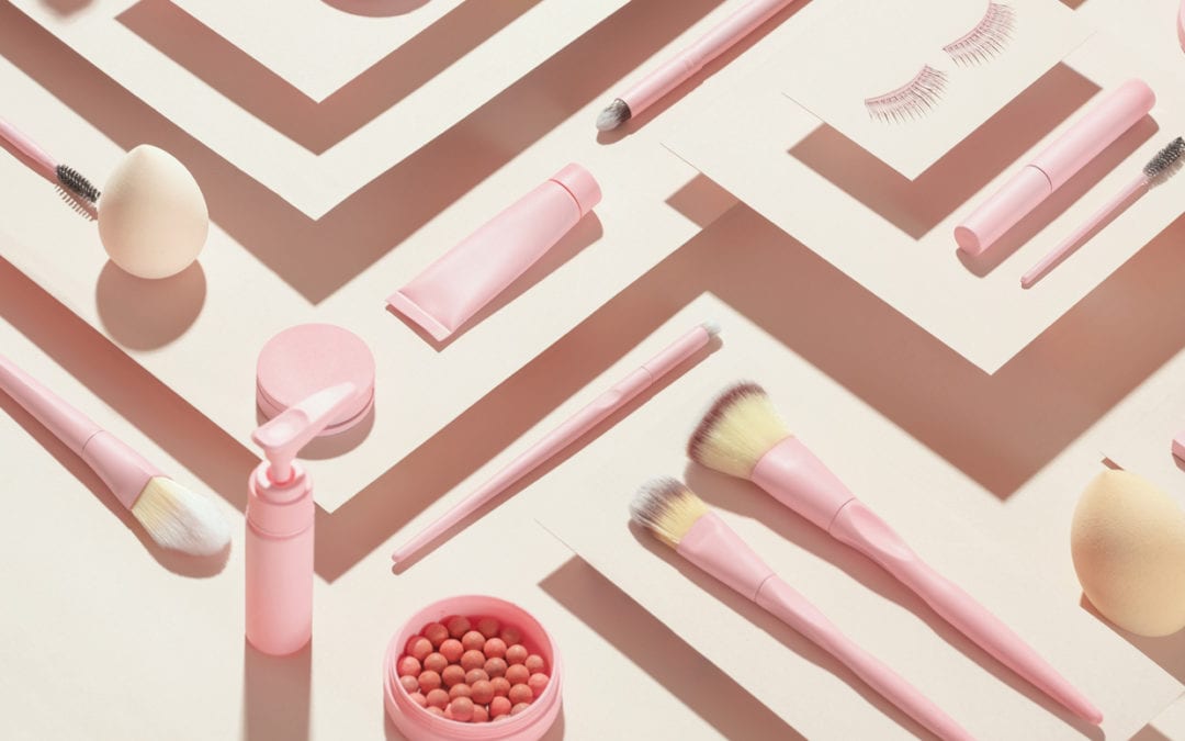 Overhead shot of pink cosmetic products on a cream background.