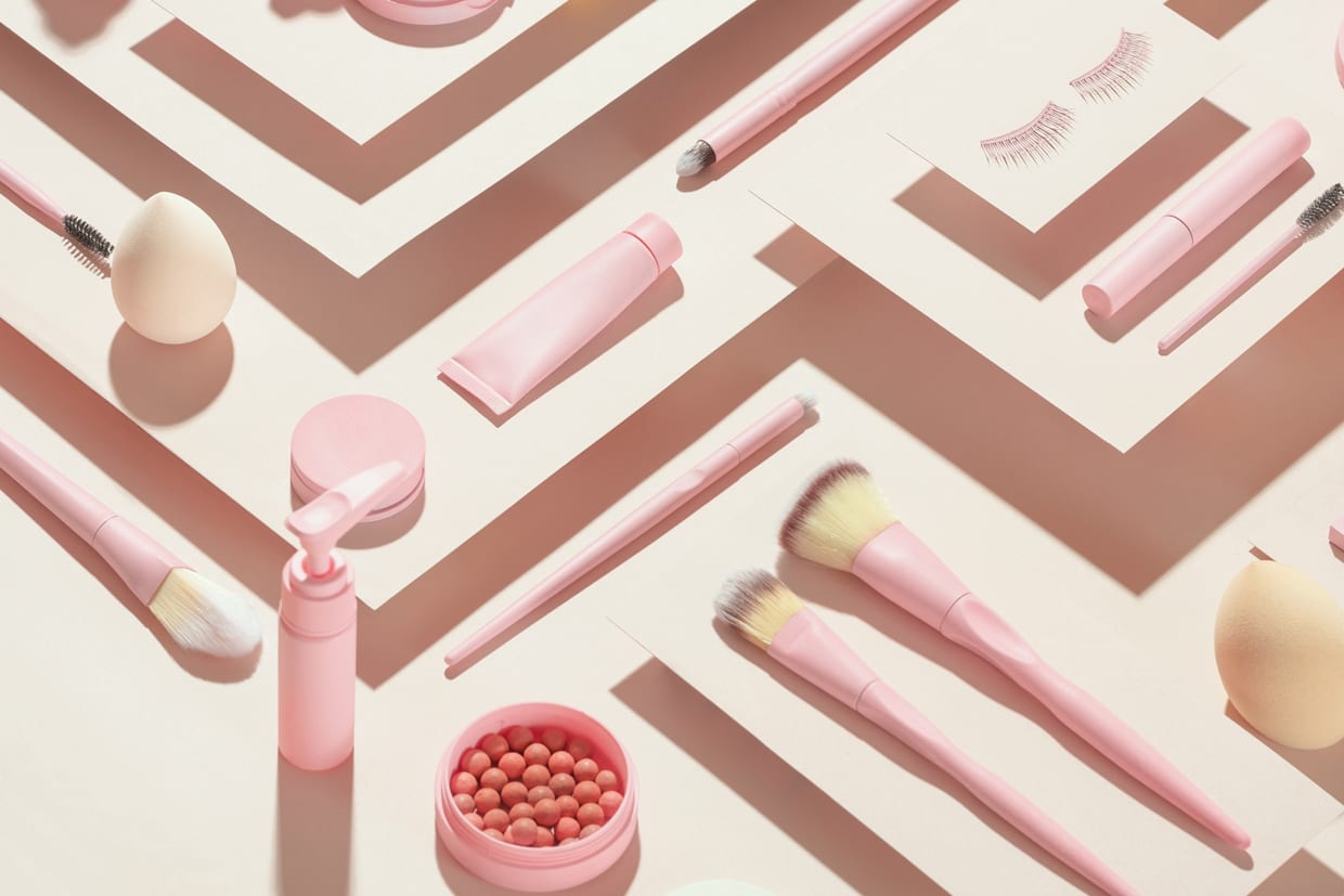 Overhead shot of pink cosmetic products on a cream background.