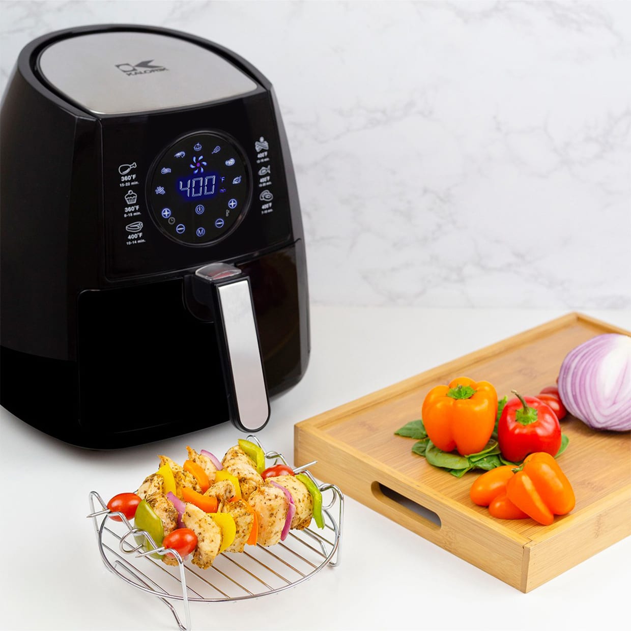 A black air fryer next to a rack and tray of vegetables.