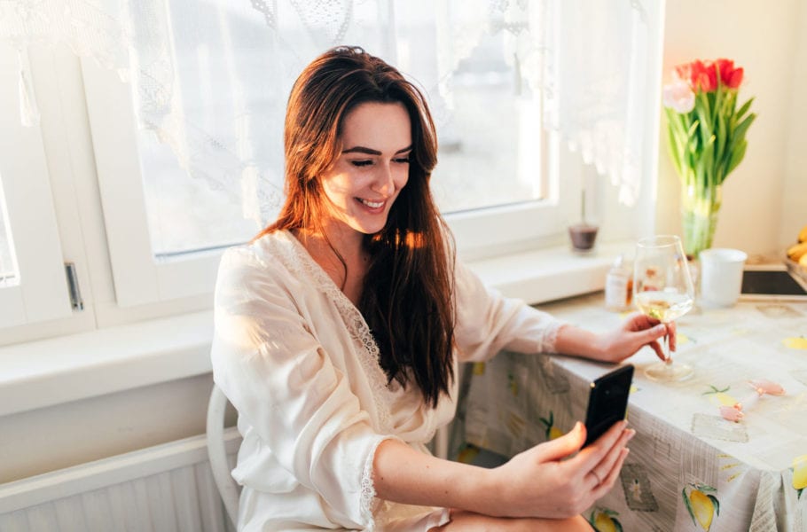 A woman holding glass of wine and using her phone.