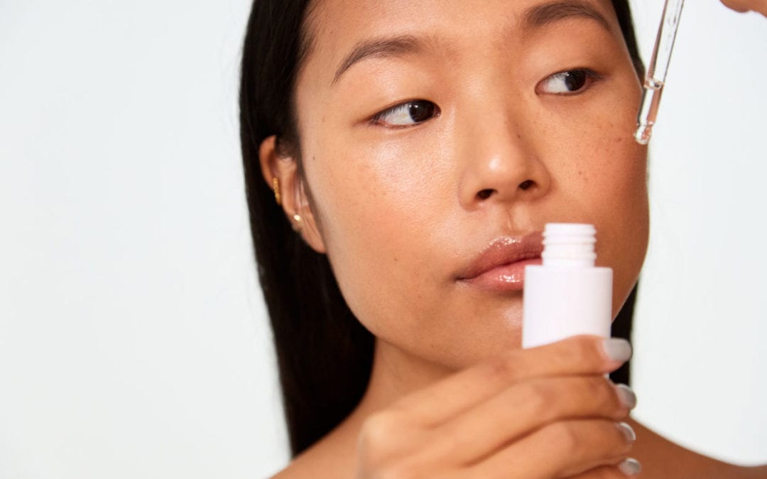 A young woman holding a dropper with skincare serum.
