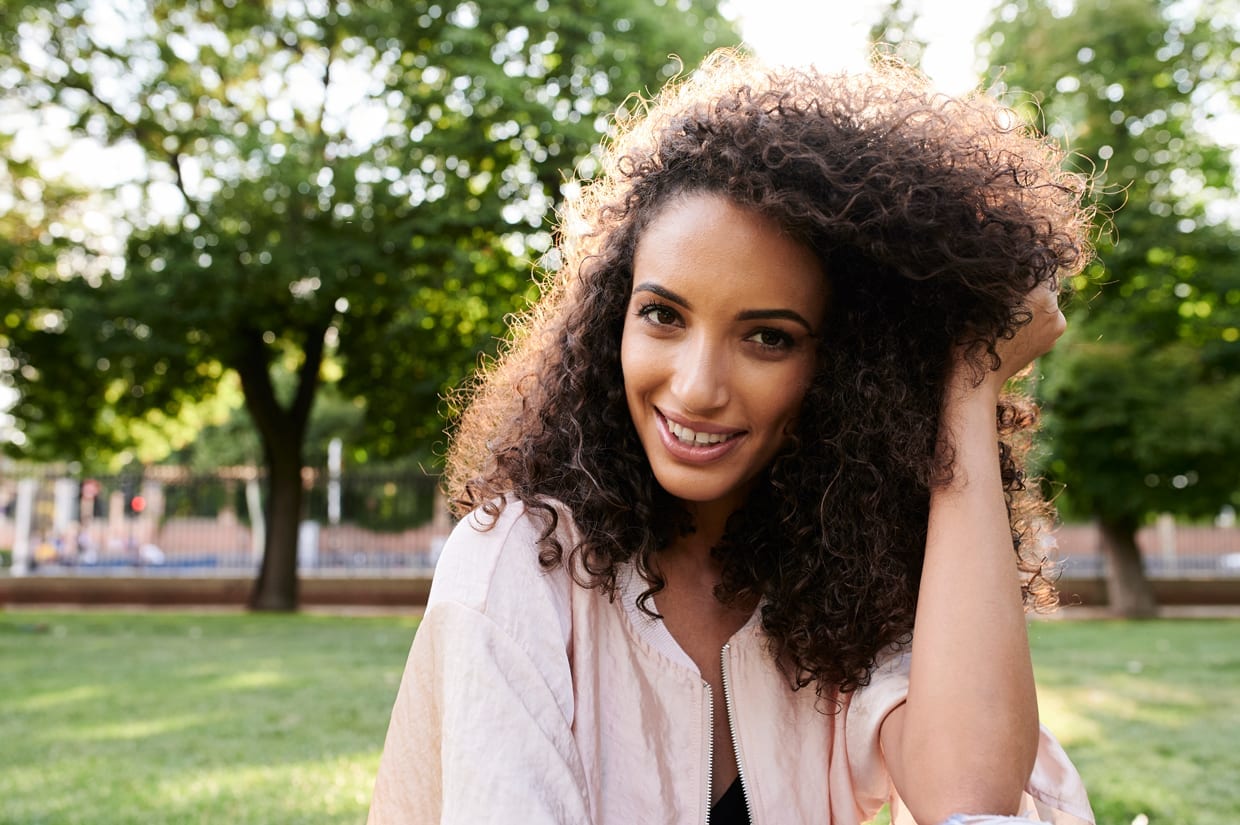 Portrait of curly haired woman looking at camera at sunset in a park.