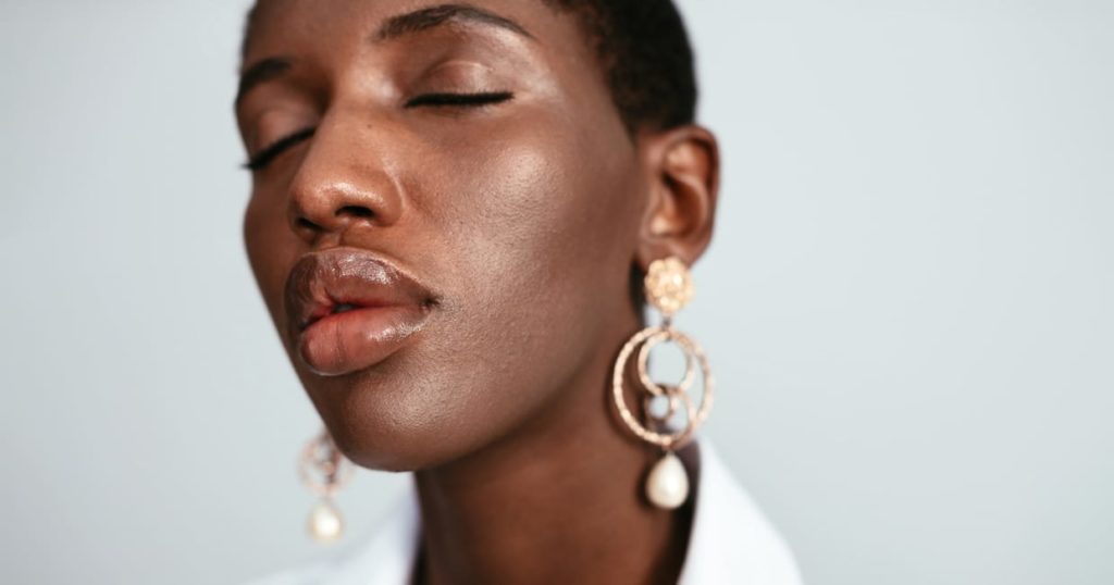 A Black woman with short hair wearing stylish earrings with her eyes closed.