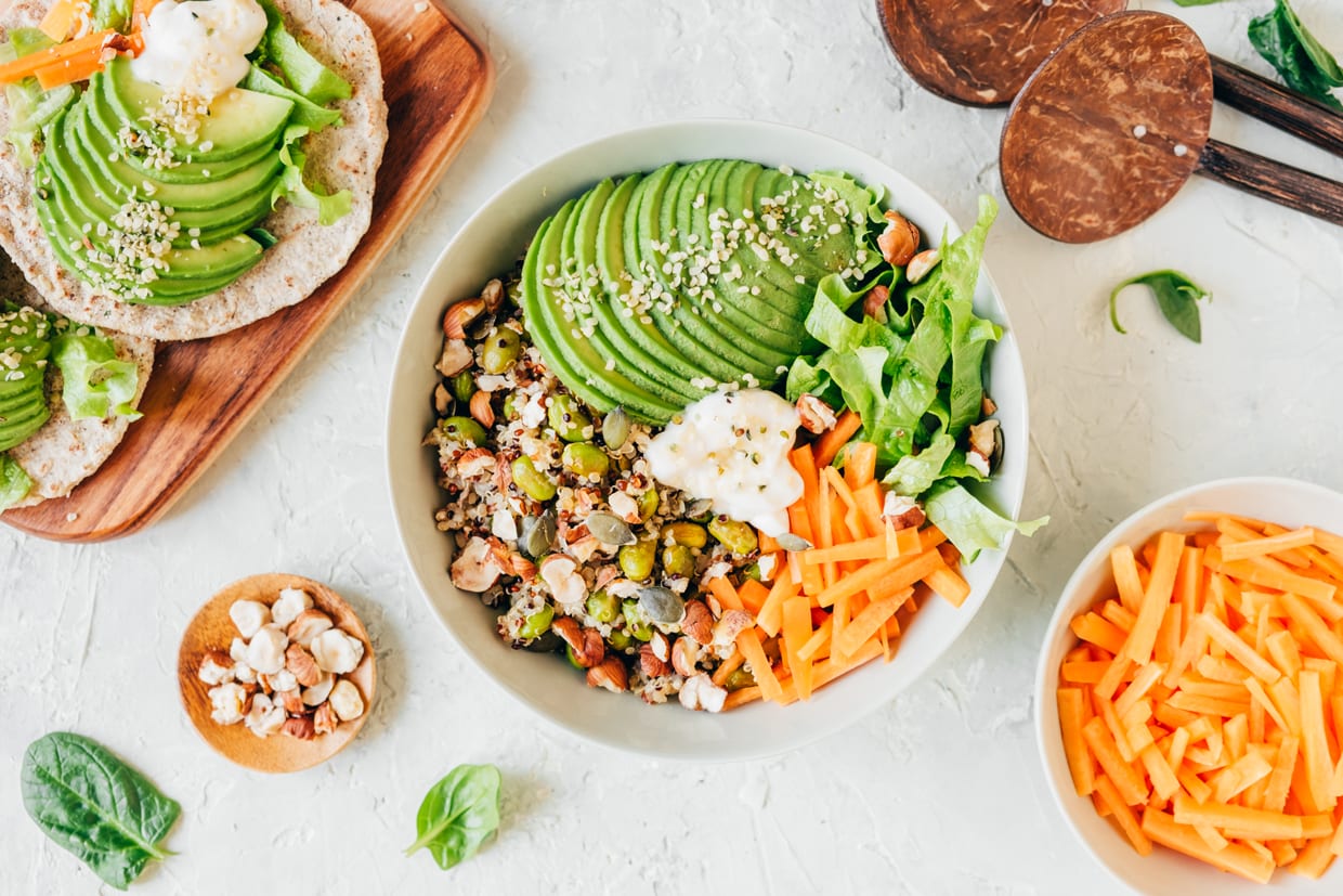 An overhead shot of a vegan bowl with quinoa, avocado, edamame, carrots, hazelnuts and pumpkin seeds.