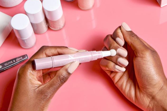 A Black woman's hands using a pen to apply a serum to her nails.