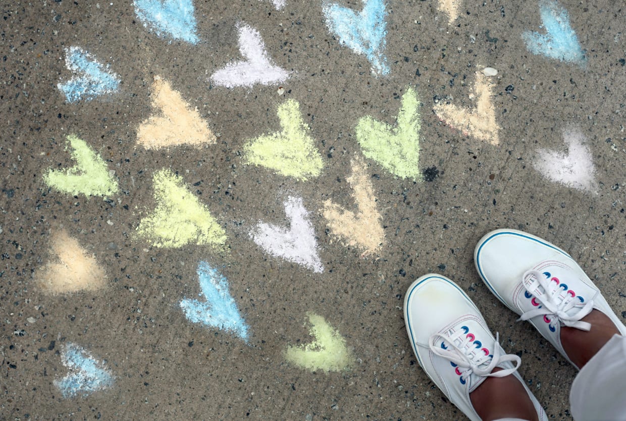 An overhead shot of a person's feet next sidewalk chalk art of hearts.