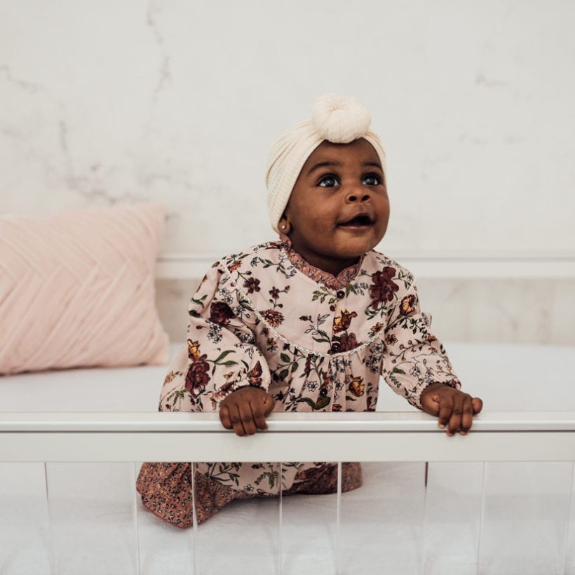 A baby girl in a crib laughing and smiling.