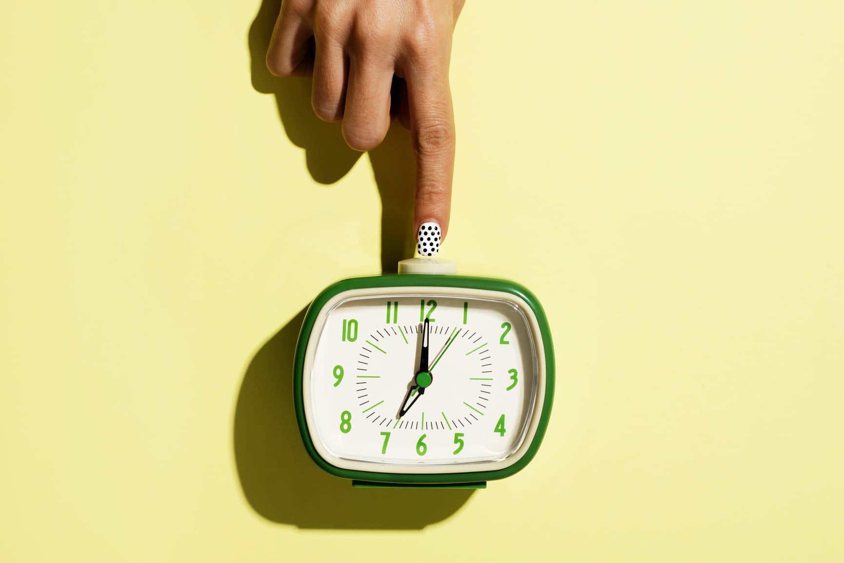 woman turning off a retro alarm clock on a yellow background