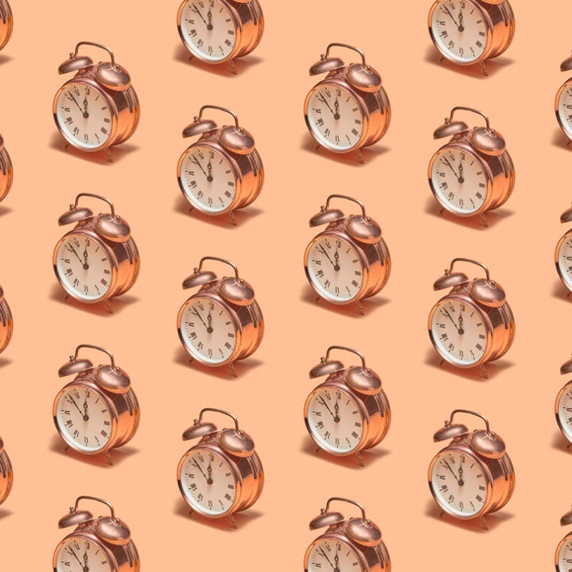 Old-fashioned copper alarm clocks on a light beige background with shadows.