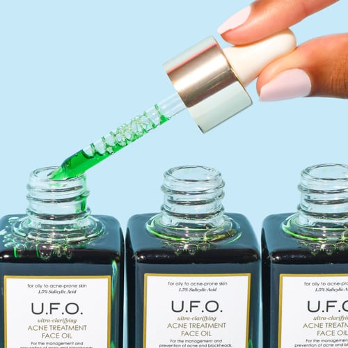 A hand holding a dropper of above three bottles of salicylic acid based skincare.