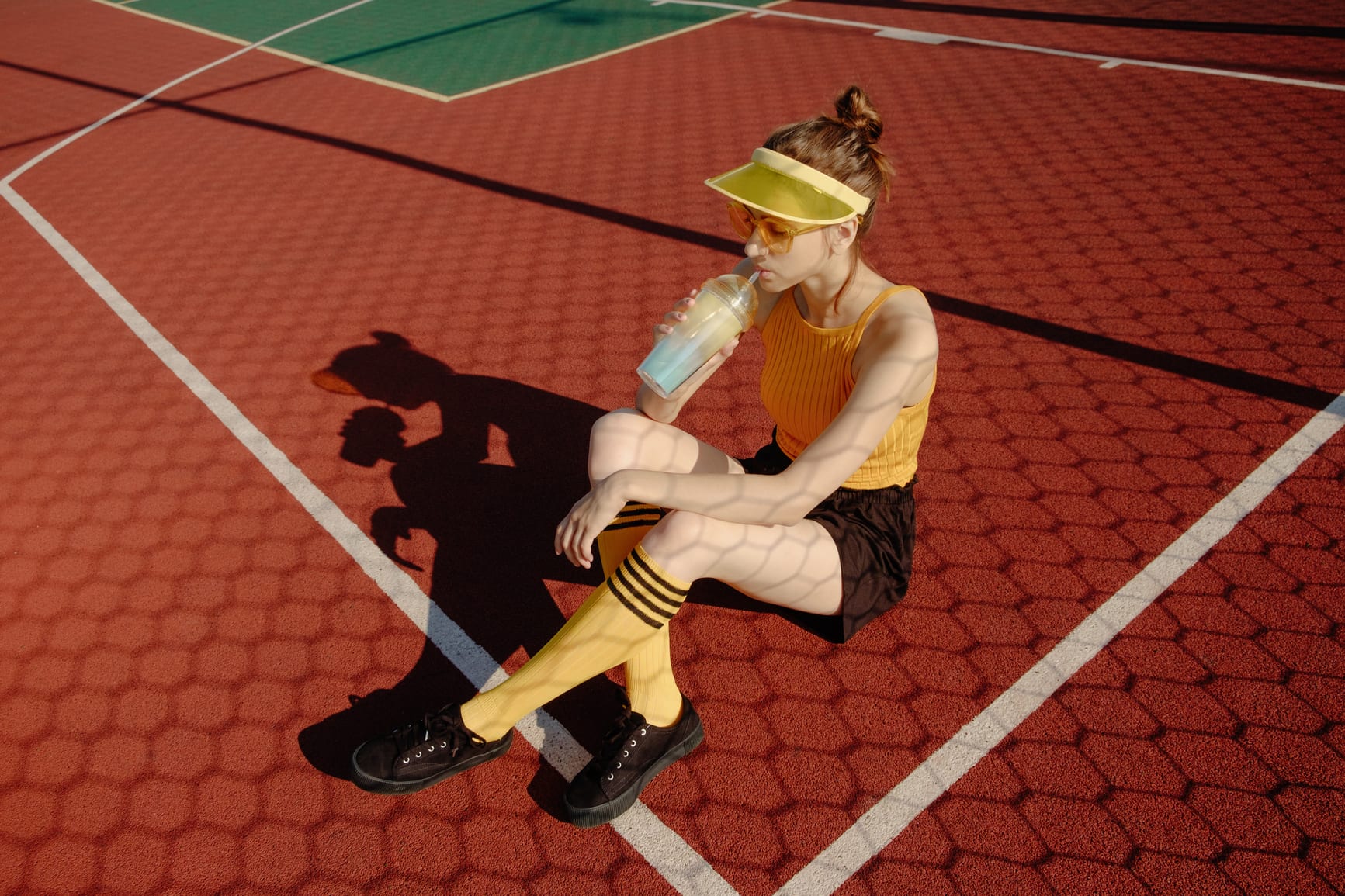 Young brunette woman in trendy sportswear sitting, drinking and taking rest on the red playground