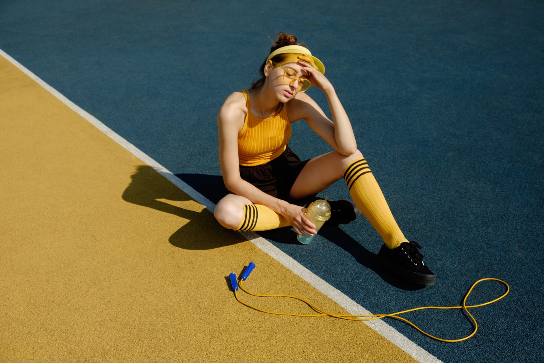 Young brunette tired woman in trendy sportswear with jump rope sitting and taking rest on the playground