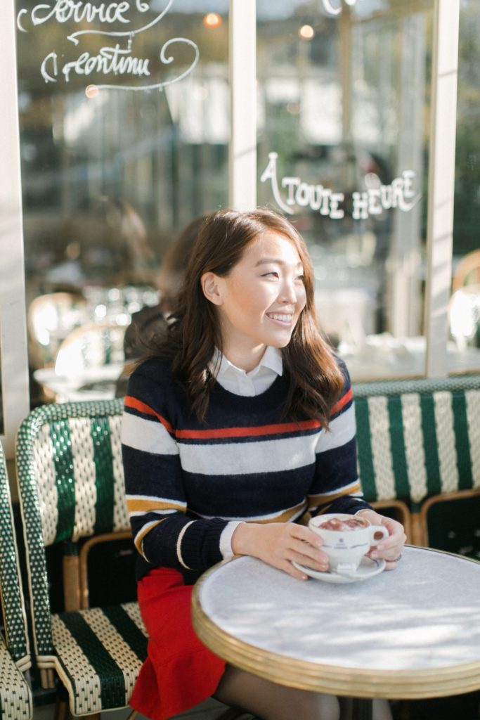 Asian girl seating outside French bistro and drinking coffee