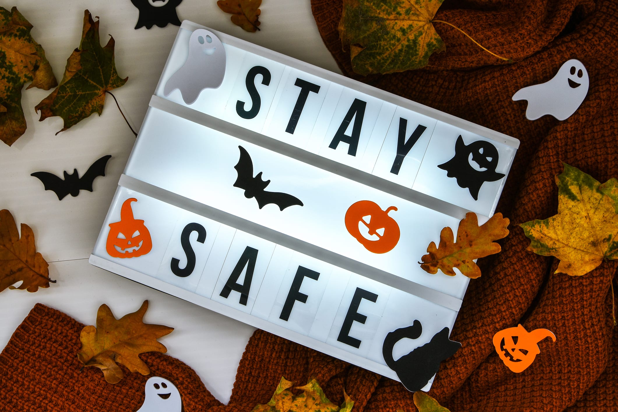 Stay safe. Text in white light box, with a background of sweater, dried leaves halloween autumn decoration. Coronavirus devices. Social distancing. Protection against pandemics. Cozy home