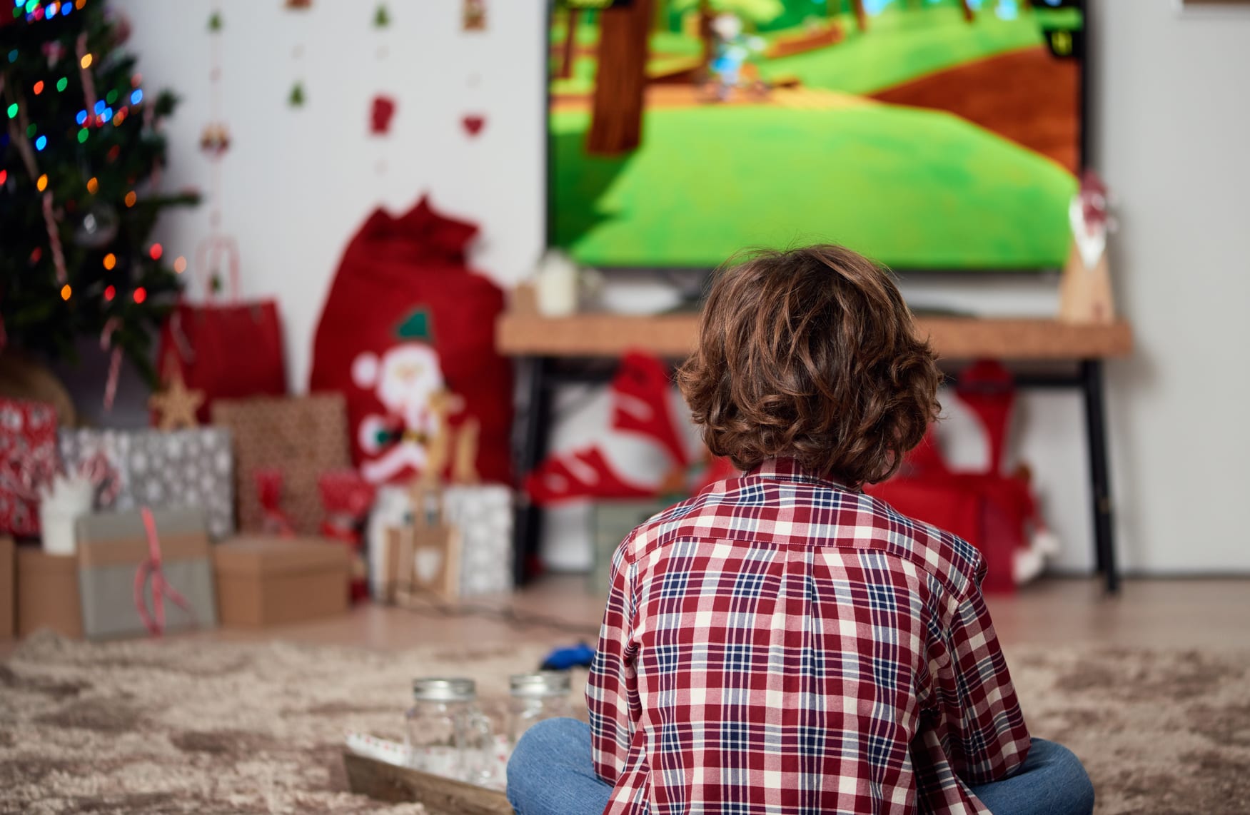 Back view of child with curly hair playing video game on TV.