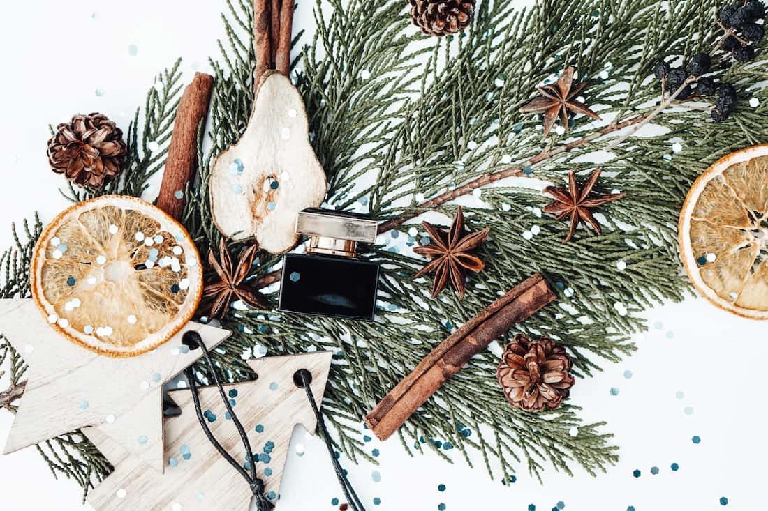 Christmas composition with evergreen tree branch, new year wooden toys, perfume bottles, dried fruits and plants, star anise cinnamon on white background.