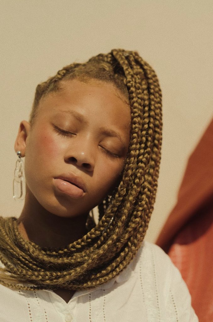 Young girl with blond, braided hair photographed in sunny, natural light.