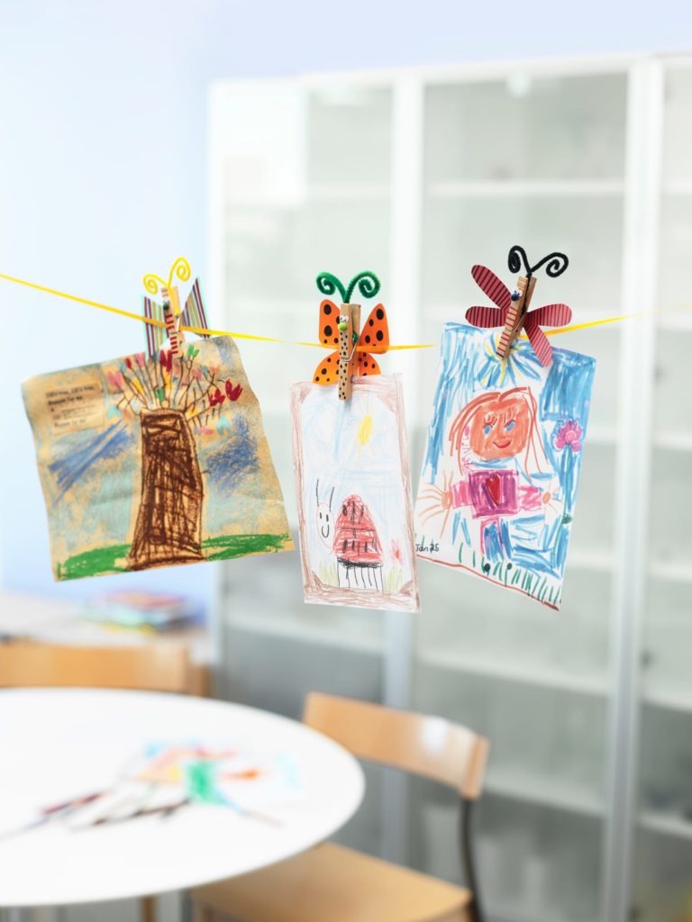 Kid's drawings displayed on a line with butterfly clothes pins.