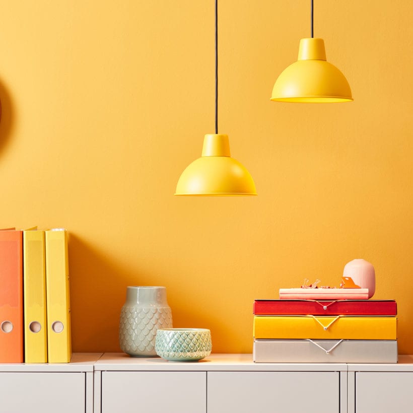 Creative interior of bright office with yellow wall and vivid folders composed on white cabinet under lamps