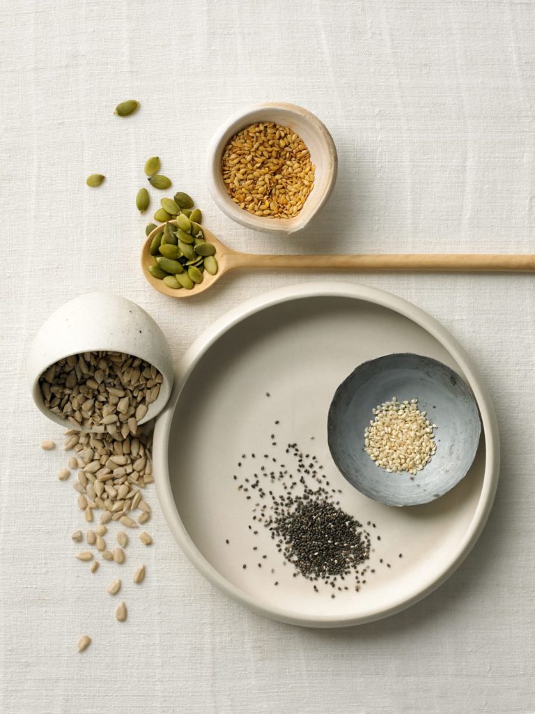 variety of edible seeds and nuts in small bowls arranged on table cloths