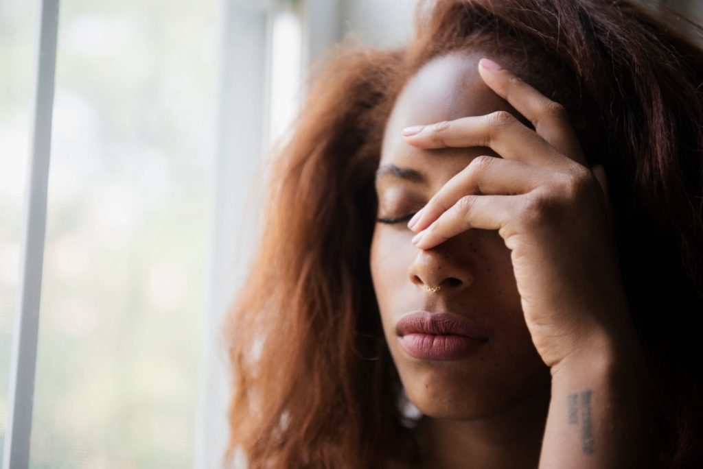 Woman holding her hand to her head in pain next to window