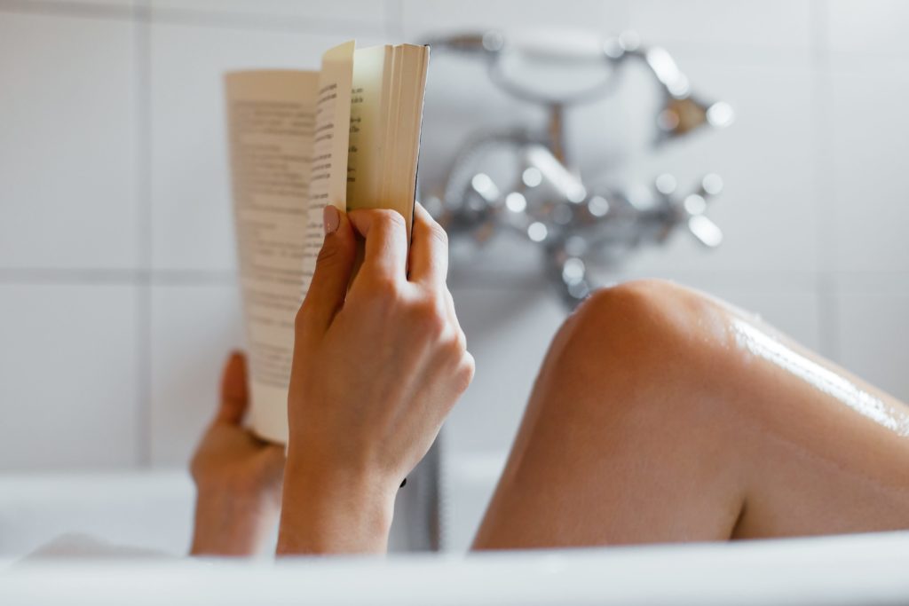 Closeup of anonymous woman reading a book in bath.