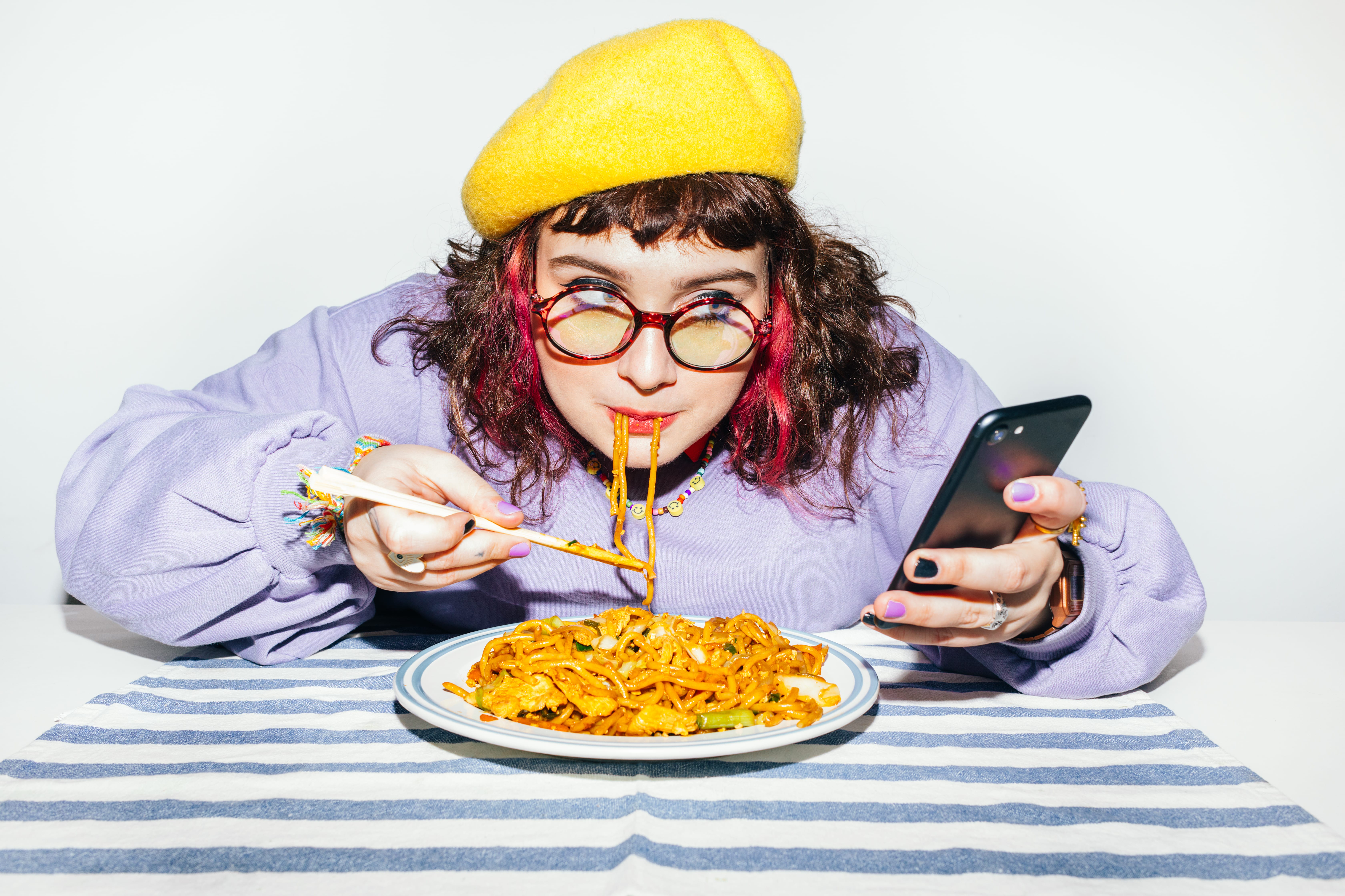 A portrait of a cute young plus size girl eating chinese food and using a mobile phone, texting
