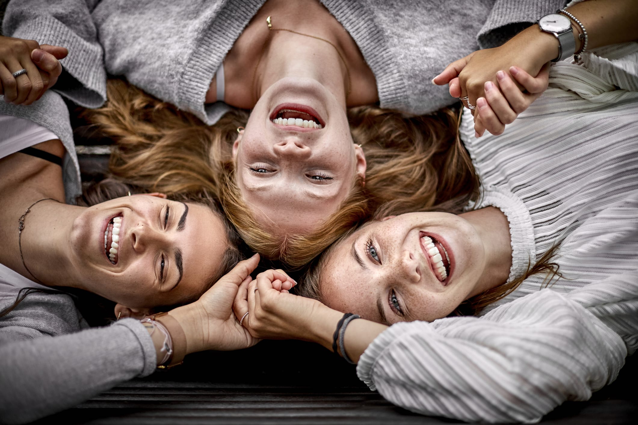 Three happy young women lying on a bench holding hands