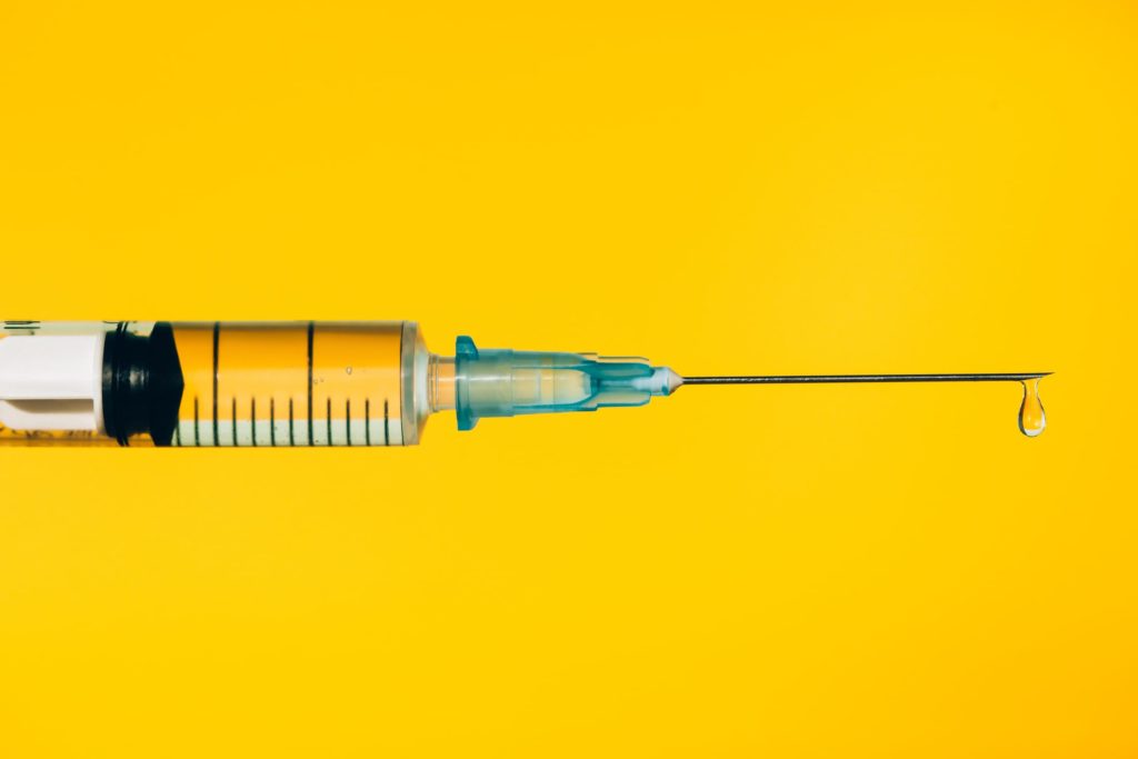 Closeup contemporary disposable syringe with drop of fluid medication on needle placed against vivid yellow background. Vaccination is the most anticipated procedure of the year. Research of coronavirus disease protection concept. Covid-19 vaccine studies.
